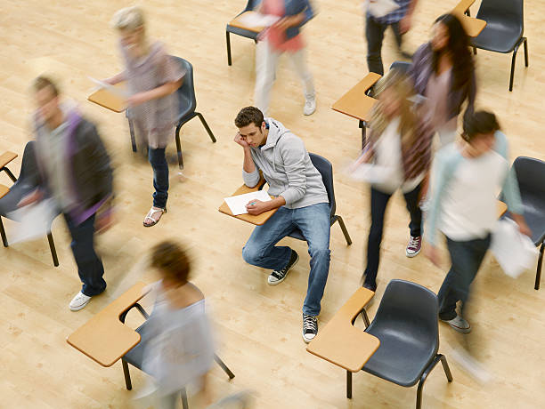 Student sits in a classroom surrounded by others moving forward before he does. The pressure of getting ahead races but the suffocating feeling of uncertainty leaves him seated. Sourced from Ghetty Images