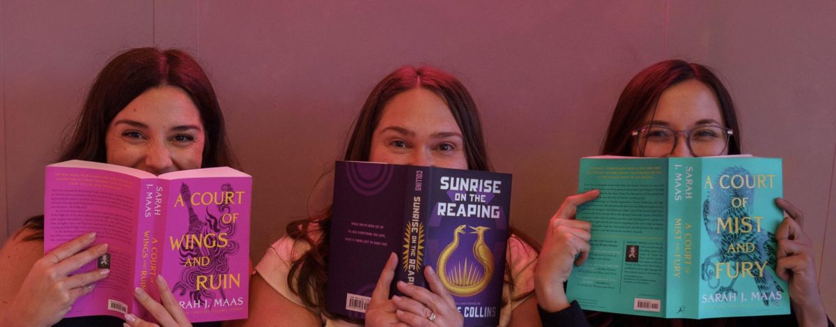 (Left to right) Samantha Mooneyham, Alison Bogatz, and Alisa Block sit inside All Booked Up, faces half covered by books.